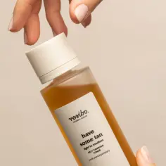 Dłoń trzyma buteleczkę toniku samoopalającego z dihydroxyacetone. Efekt muśnięcia słońcem.