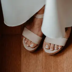 Stopy w sandałach, z idealnym pedicure french. Delikatne paski sandałów i biel sukni tworzą subtelny kontrast.